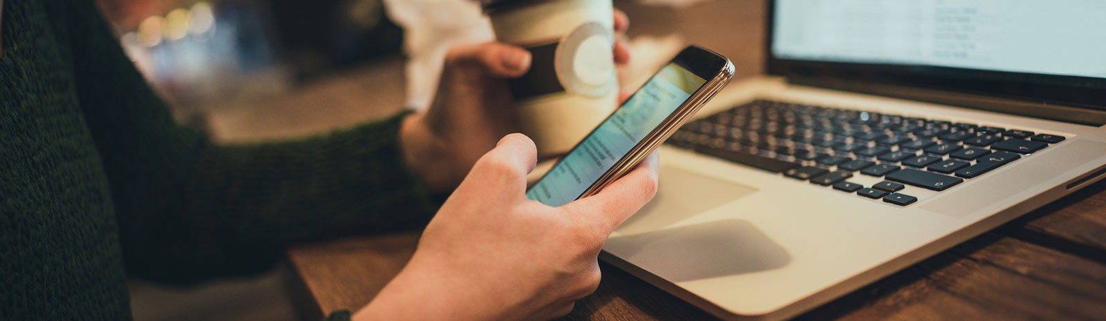 a person holding a cup of coffee in one hand and their mobile device in the other